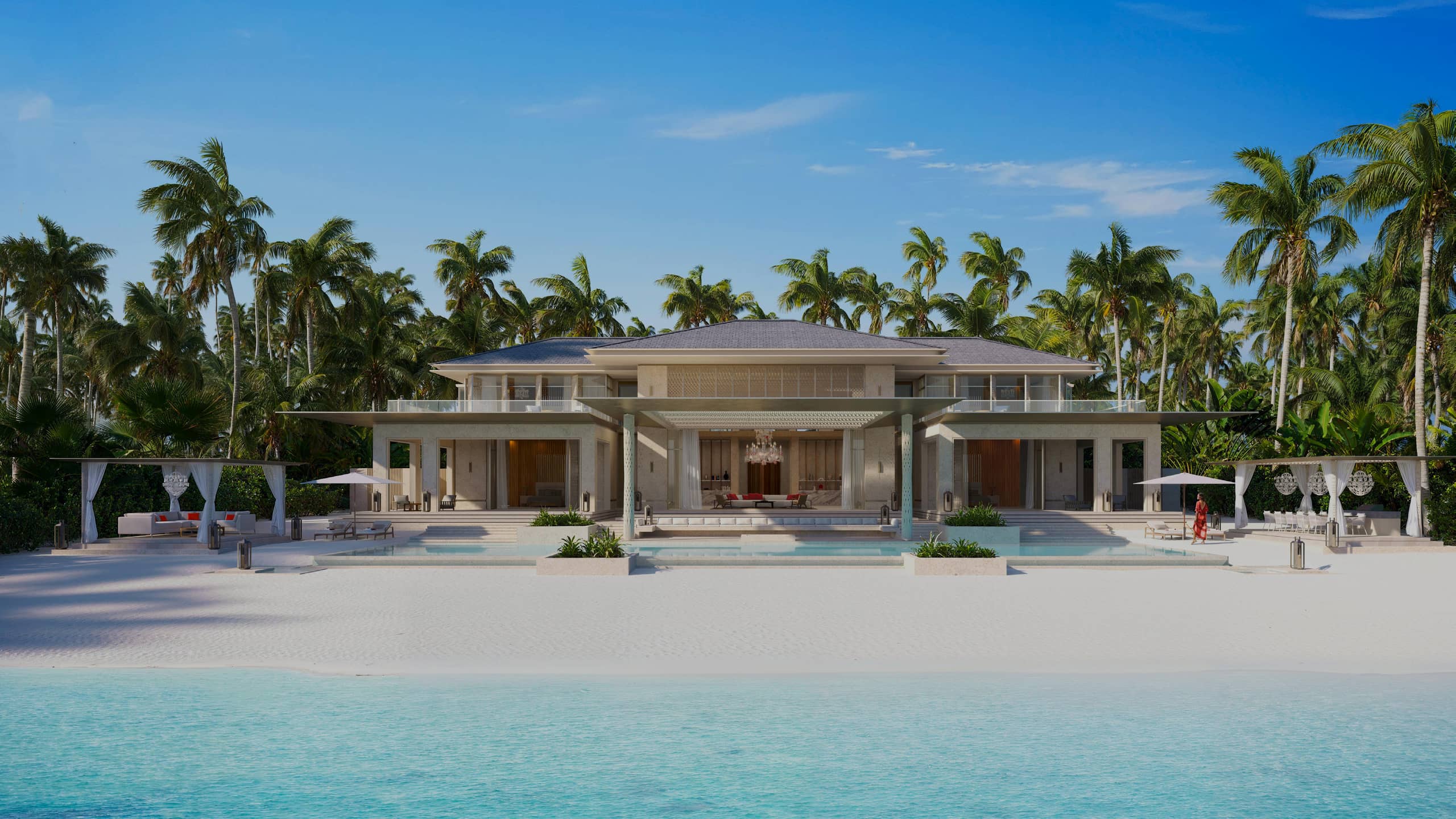 A two-storey beachfront villa among palm trees, its pool terrace facing white sand and turquoise water
